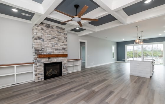 Great room with a coffered ceiling in navy and white, a stone fireplace, and white built-in shelving either side