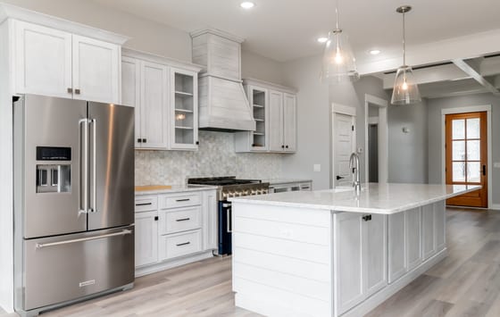 Kitchen seen from the dining end, with whitewashed cabinetry, hexagonal tile backsplash, and a wood front door beyond