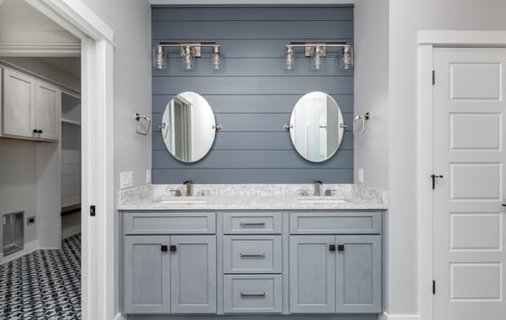 Double vanity with oval mirrors and glass sconces against a navy shiplap wall, over patterned floor tile